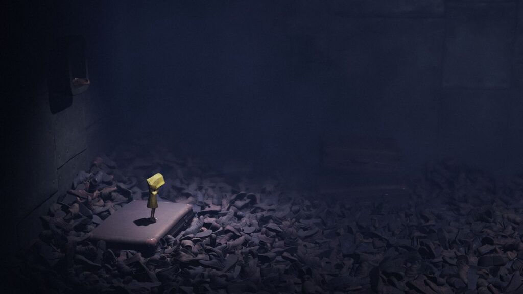 Feature image for our Little Nightmares Android news piece. It shows Six stood alone in a room full of abandoned shoes.