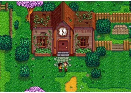 The image shows a screenshot of the in-game play of Stardew Valley. Two characters in a pixel-style face one another in assumed friendly conversation. Behind them is a grand building that looks weathered with vines growing across it, a large clock in the centre of the building highlights its presence. The surrounding scenery is of course pixelated too, and very lush with grass, path, and foliage. The trees are gorgeous and green. It must be summer!
