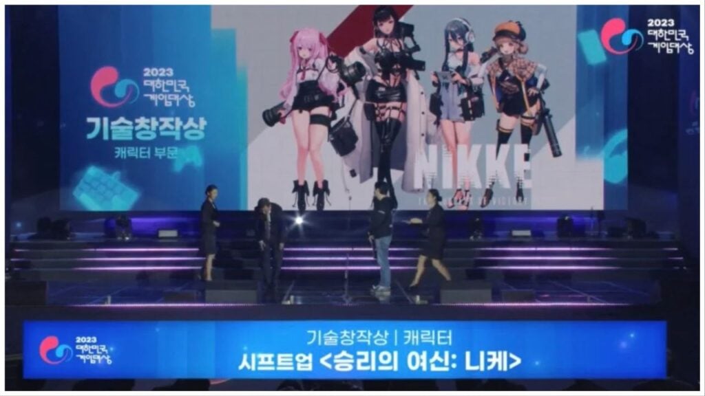 feature image for our nikke g-star awards news, the image features a screenshot from the broadcast of the awards show, with 4 people on the stage, as one bows, there is a screen behind them with 4 characters from the game
